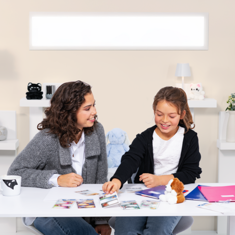 Deux filles sont assises à une table, entourées de photos et de fournitures de bureau, tandis qu'elles discutent et rient ensemble.