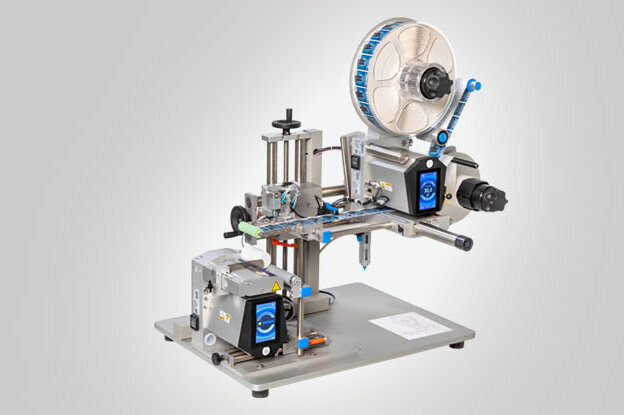 Une machine à étiqueter avec différents composants pour appliquer des étiquettes sur des produits. Elle est montée sur une table stable.