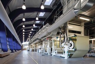 Texte : "Salle de production moderne avec de grandes machines pour le traitement des matériaux, une lumière vive et des plafonds hauts.