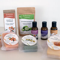 Étiquettes sur différents produits cosmétiques : Doypacks avec du lait de bain et de la poudre de bain, bouteilles en verre brun avec des arômes de bain, ainsi que des savons à l'huile végétale avec des étiquettes rondes dans des sachets transparents, sur fond clair.