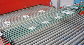 Des plaques de verre sont transportées sur un tapis roulant, avec plusieurs étiquettes visibles pour leur identification.