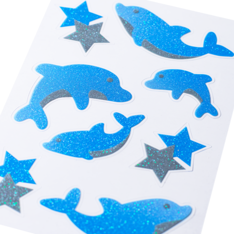 Autocollants pailletés bleus en forme de dauphins et d'étoiles sur fond blanc.