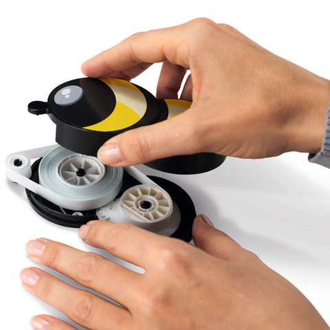 Une main tient un dérouleur jaune et noir, tandis qu'une autre main tire sur la ficelle.