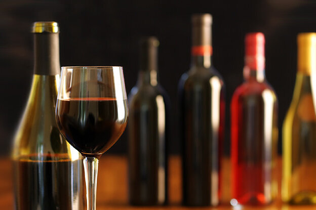 Un verre de vin rouge est posé devant plusieurs bouteilles de vin de différentes couleurs sur une table.