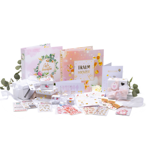 Hochzeitsplanungsset mit zwei Fotoalben, Geschenken, Aufklebern und Dekorationen in Pastellfarben, umgeben von Eukalyptusblättern.