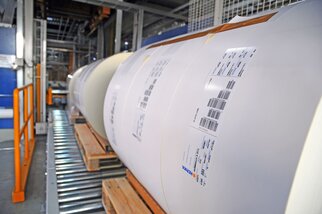 Des rouleaux de papier sur un convoyeur, chacun portant une étiquette contenant des informations et des codes-barres.